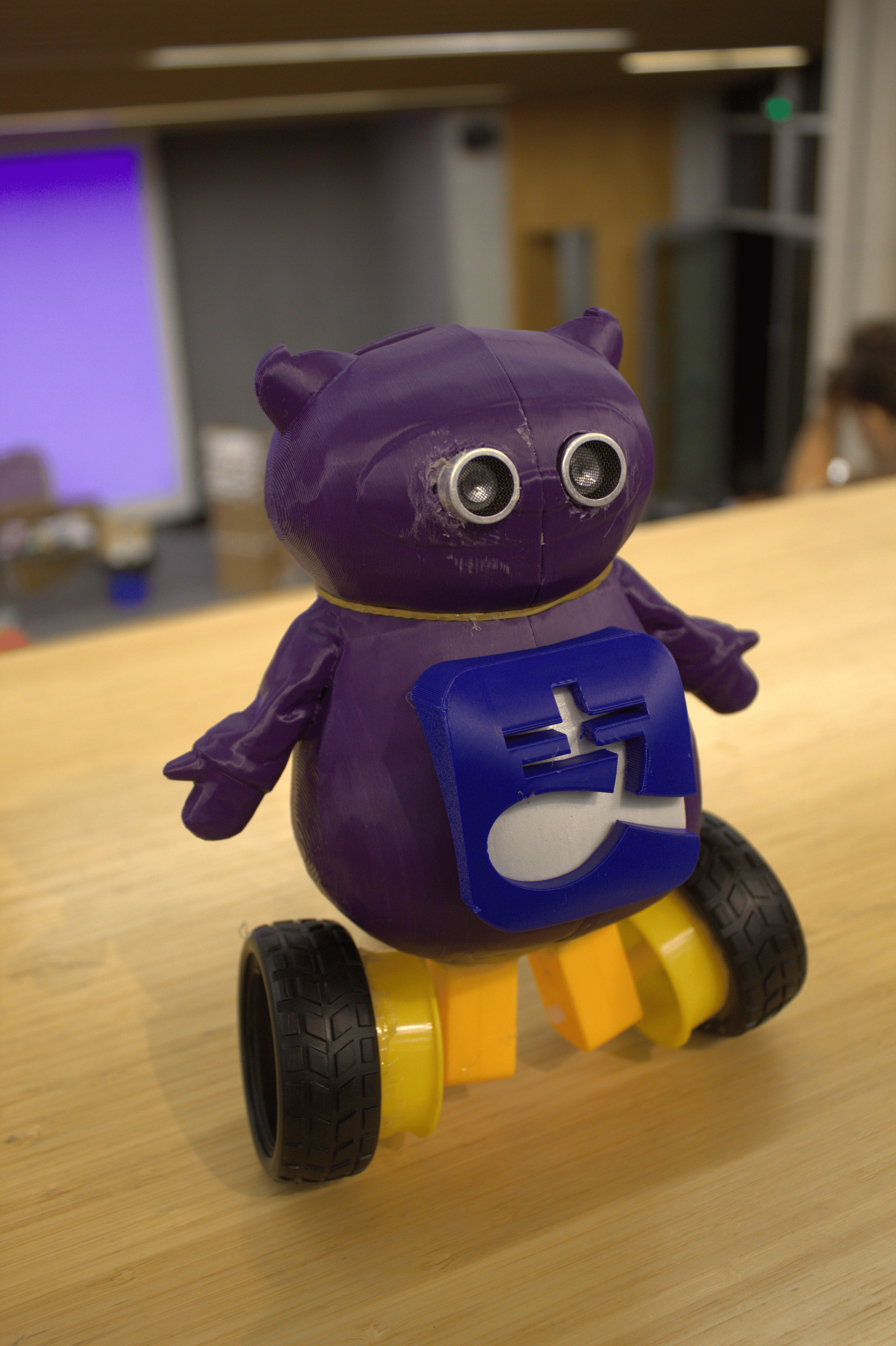 Photo of the purple AliPayBot prototype from the side, showing its yellow wheels and blue front panel.