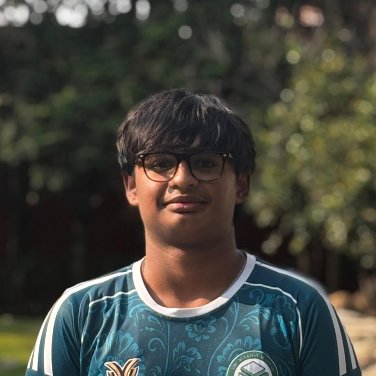 Outdoor portrait of a young man wearing glasses and a teal sports jersey.