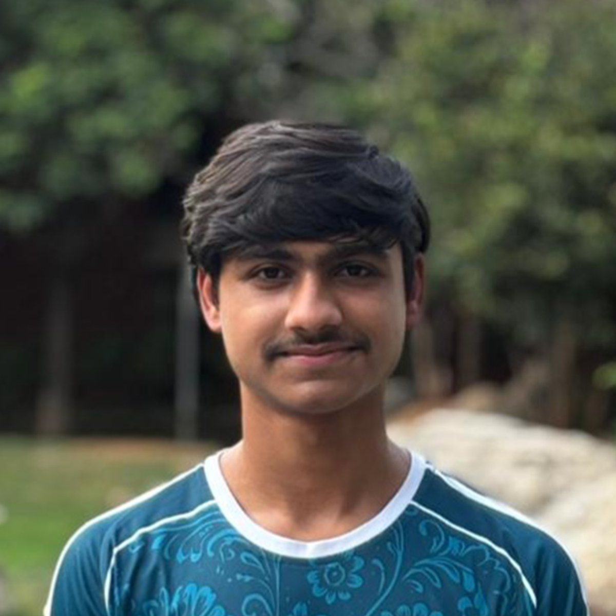 Outdoor portrait of a young man in a teal patterned sports jersey.