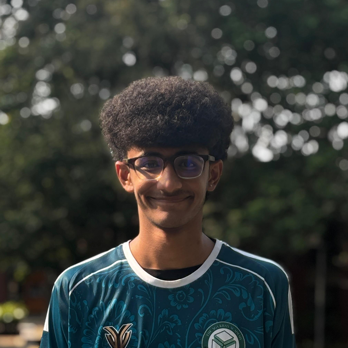 Outdoor portrait of a young man with curly hair and glasses wearing a teal jersey.